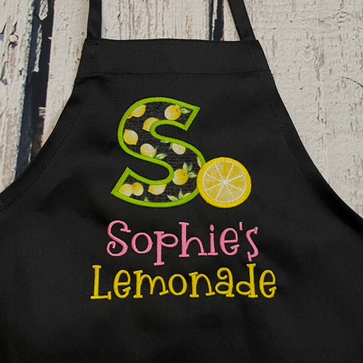 Child's embroidered personalized lemonade stand apron with their initial and name on black apron