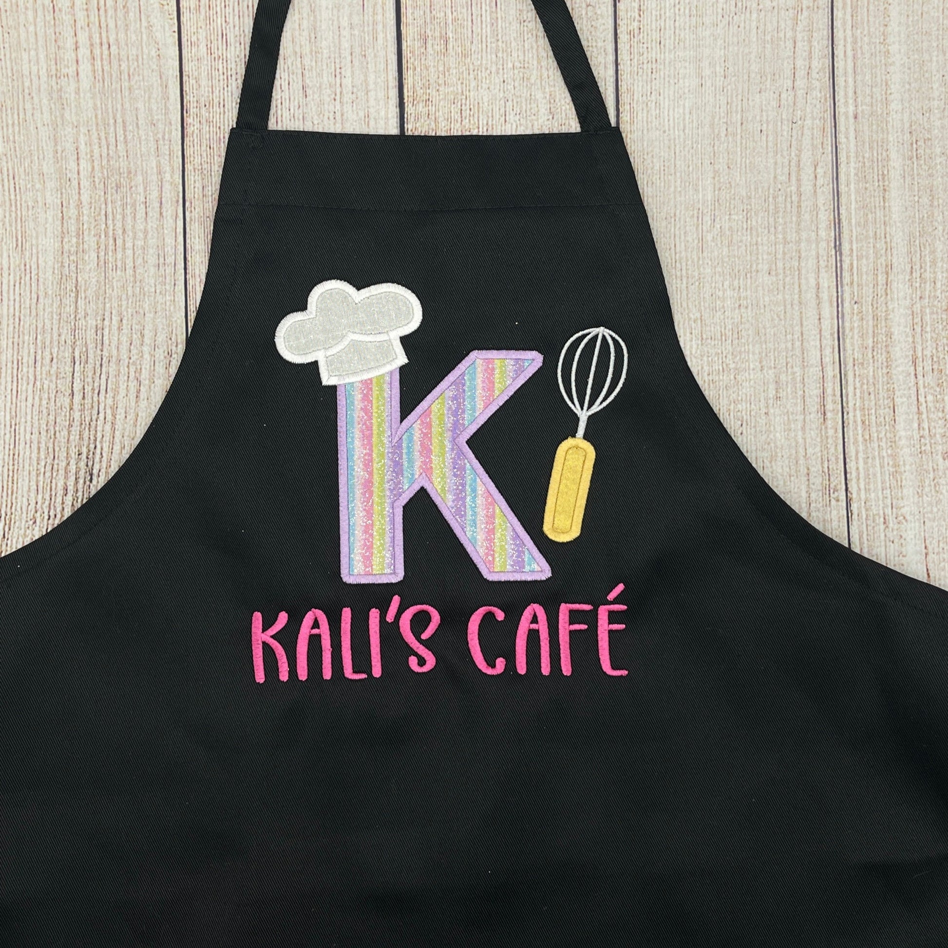 Child's personalized embroidered black apron that has a large initial and says child's name and café